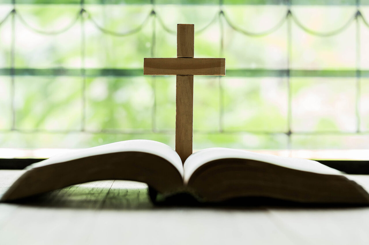 Crosses that open above the Bible on a wooden table with window lighting
